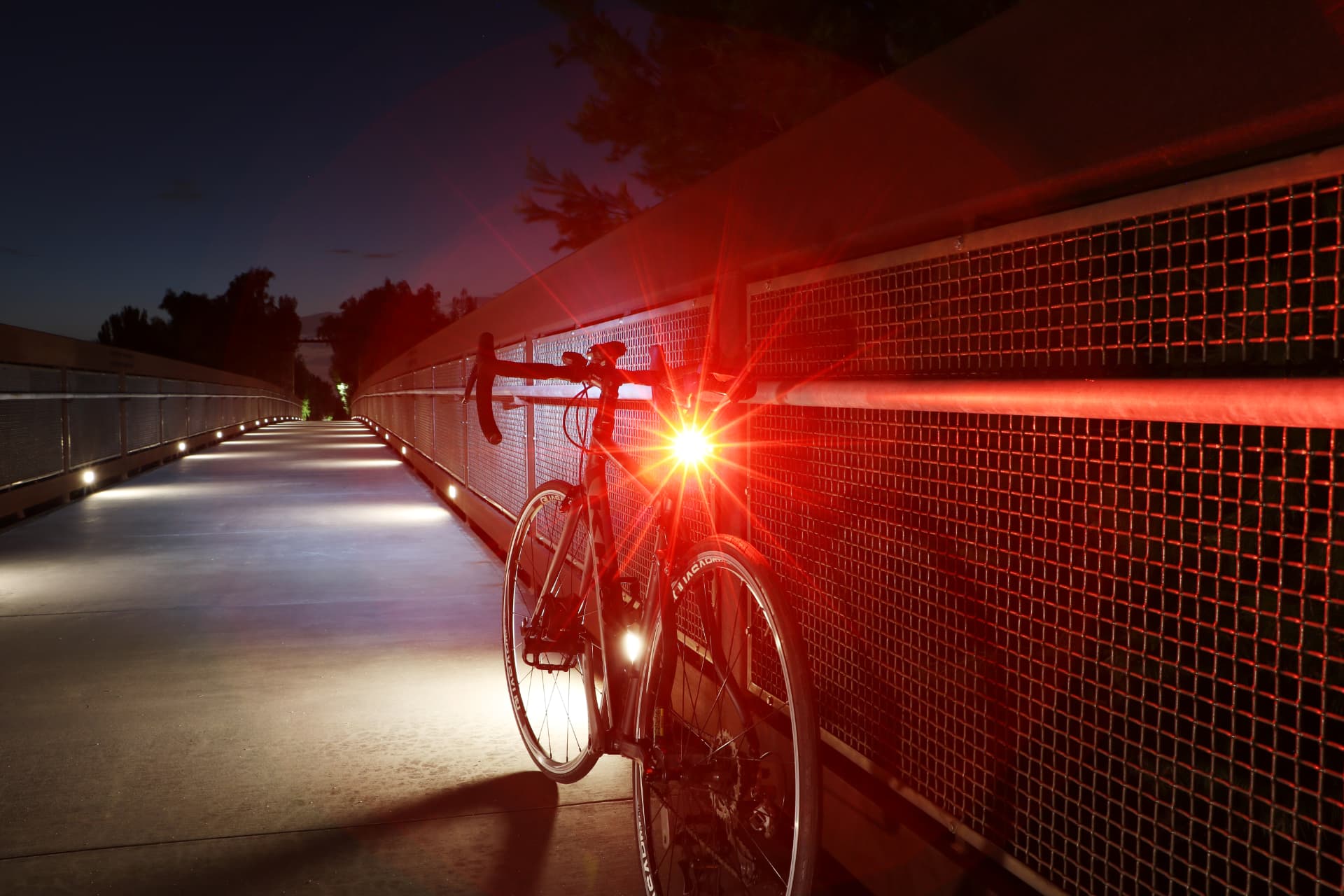 Road bike on a lit bridge path with a Cygolite Slingshot taillight glowing red
