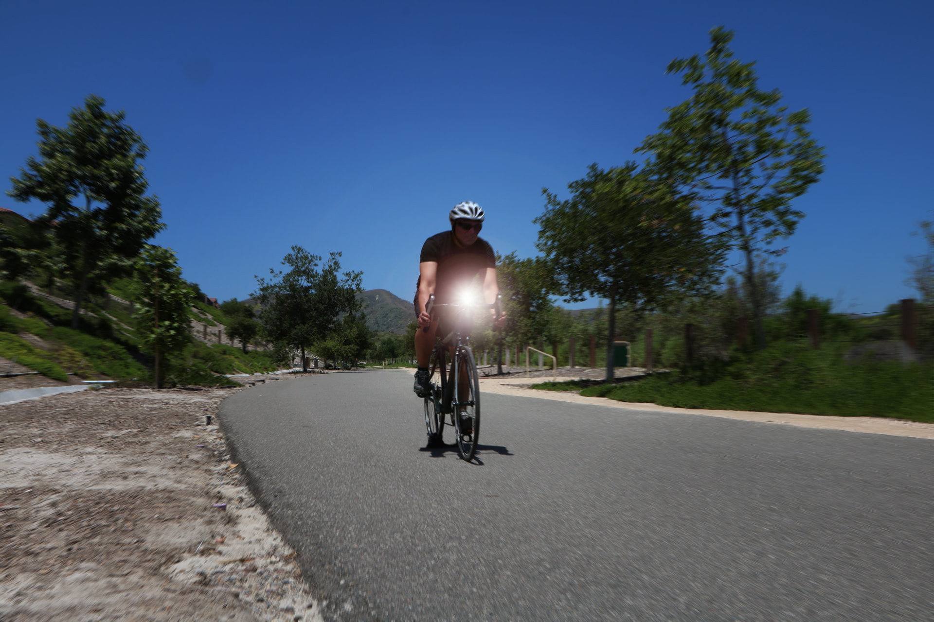 Cyclist riding on a sunny park road with a bright Cygolite headlight